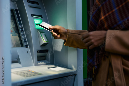 Close up of black woman using credit card while withdrawing cash at ATM.