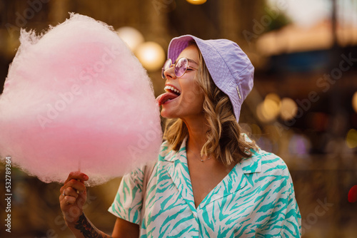 Young white woman eating cotton candy in attraction park