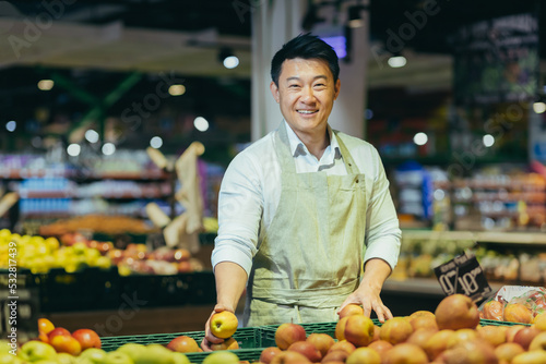 Portrait of Asian supermarket salesman, man in grocery vegetable section smiling and looking at camera.