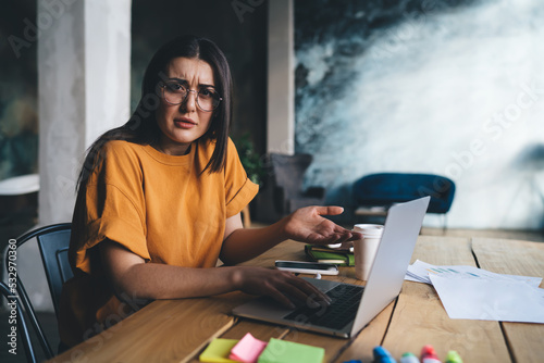 Confused young lady sitting at table with laptop