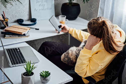 Woman freelance or procrastinate at workplace at home office. Self-employed businesswoman with cat distracted from work on laptop scrolling social media on smartphone.