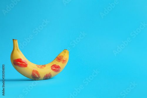 Banana covered with red lipstick marks on light blue background, space for text. Potency concept