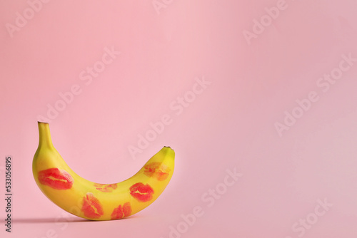 Banana covered with red lipstick marks on light pink background, space for text. Potency concept