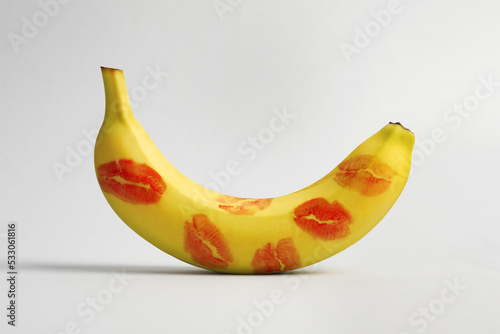 Banana covered with red lipstick marks on light grey background. Potency concept