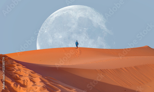 Happy bedouin in traditional bright clothing standing on sand in sahara desert with super full moon - Sahara, Morocco "Elements of this image furnished by NASA"