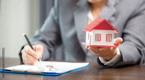 Woman home sales person is checking documents for house purchase contract before letting the customer sign contract on table is key with house model, real estate trading and insurance property concept