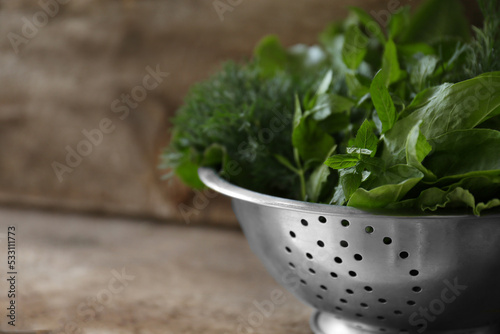 Different herbs in colander on wooden table, closeup. Space for text