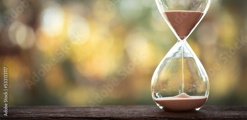 hourglass (sand clock) on an old wooden table with natural blur background, Hourglass as time passing concept for business deadline, Life-time passing concept, elapsed time concept, copy space.