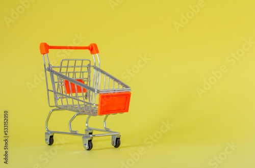 Metal shopping cart on a yellow background with a place to copy. A symbol of trade and sales.