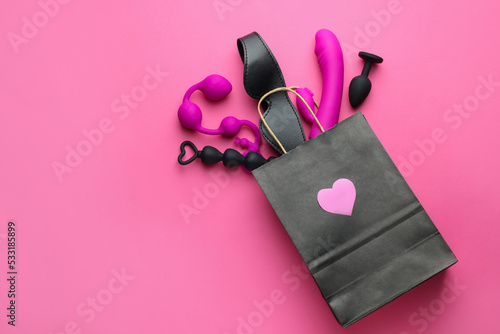 Shopping bag with different sex toys on pink background, flat lay. Space for text