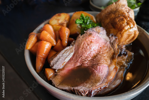 Roast beef slices on a plate with carrots, roast potatoes, a Yorkshire pudding and gravy, making a complete Sunday roast meal.