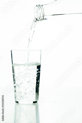 Detail of a glass bottle pouring water into a glass tumbler on a white background.