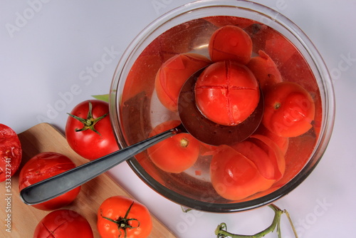 a lot of blanched tomatoes in a bowl with water, ready for peeling