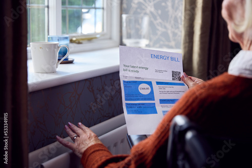 Senior Woman In Wheelchair With USA Energy Bill By Radiator In Cost Of Living Energy Crisis