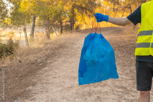 Detalle de brazo con bolsa de basura con plásticos, de un voluntario en la montaña. Fotografía horizontal con copy space.
