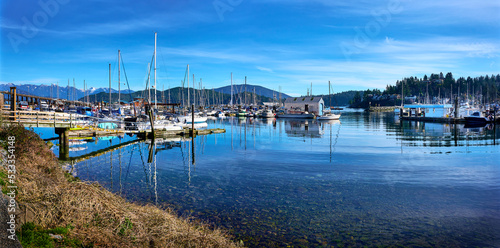 Gibsons Harbour. Yachts, boats at the piers against the backdrop of mountains in sunny weather. Gibsons, Sunshine Coast, BC, Canada