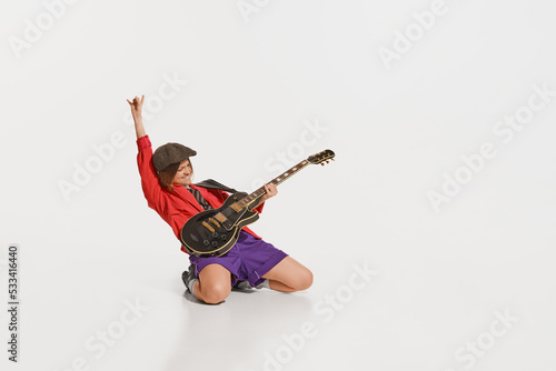 Stylish girl, retro musician wearing vintage style bright clothes playing guitar like rockstar isolated on white background.