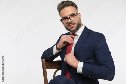 arrogant young businessman sitting on chair and adjusting red tie