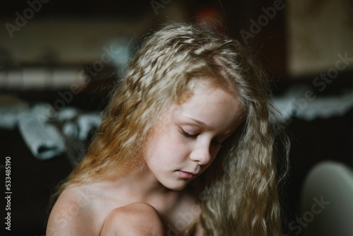 close-up portrait of a pensive, sad little girl with long curly hair at home