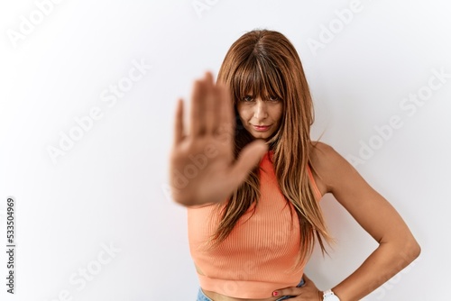 Hispanic woman with bang hairstyle standing over isolated background doing stop sing with palm of the hand. warning expression with negative and serious gesture on the face.