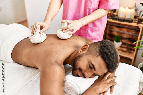 Young african american man reciving herbal pouches thai massage at beauty center.