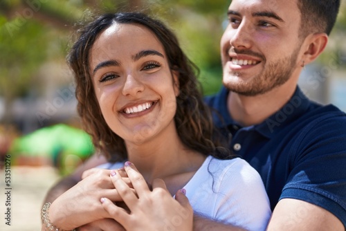 Young hispanic couple smiling confident hugging each other at park