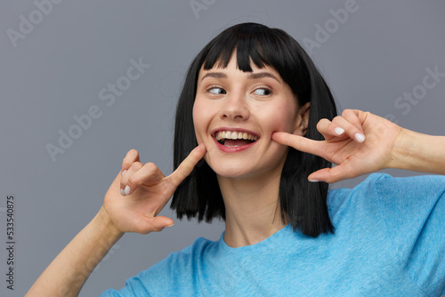 a close photo of a funny, funny, emotional woman in a blue T-shirt on a grey background making a funny grimace