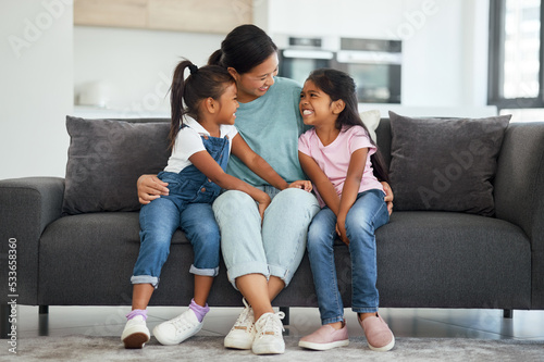 Family, love and single mother with kids looking happy, relax and smiling sitting together and bonding on sofa in lounge at home. Asian babysitter woman hugging cute girls, daughters or twin sisters