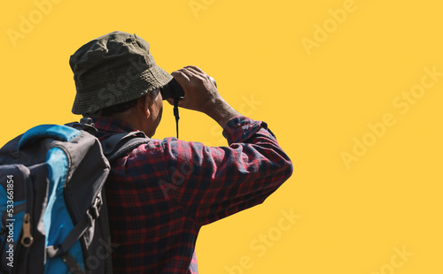 A man tourist exploring a forest and using professional binoculars isolated on yellow background with clipping path.
