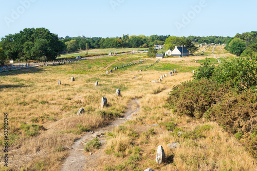 Aerial horizontal view of the mysterious rows of megalithes (menhir) in the archeological site of Carnac, Brittany, France, with a traditional cottage. Blue sky on the background.