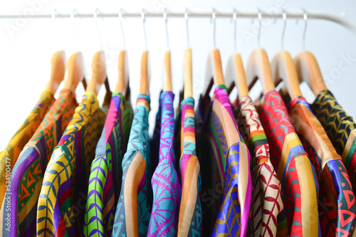 Close up collection of colorful woman blouse hanging on wooden clothes hanger in closet or clothing rack over white background, copy space.
