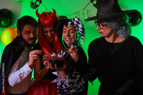 Four people look disgusted at a candy worms at a costume Halloween party.