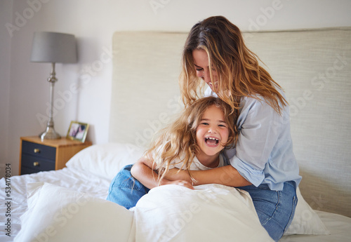 Mom and child on the bed playing together, having fun and laughing. Portrait of mother and daughter in bedroom, smiling while woman tickle young girl. Family, love and laughter in morning at home