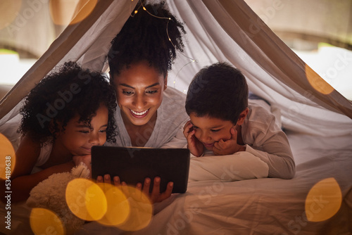 Family, tablet and online streaming with kids for a bedtime story, movie or cartoon for educational fun while in a blanket fort. Brazilian woman with boy and girl child at night reading on internet