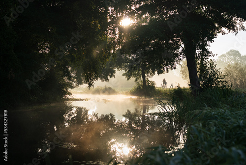 A woman cycling along a canal in the countryside during a foggy morning in autumn.