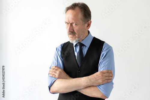 Portrait of suspicious mature businessman looking at camera. Senior Caucasian manager wearing formalwear standing with folded arms against white background. Suspicion concept