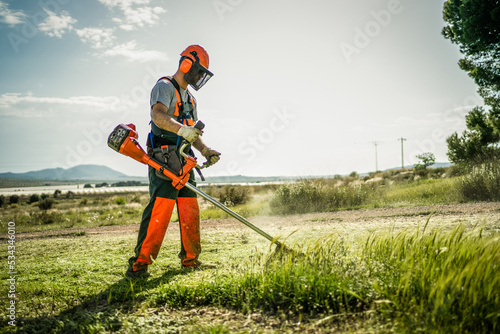 Backlit side view of a man removing grass with a trimmer