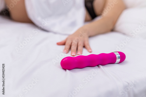 Woman in bed under sheets holding vibrator in hand