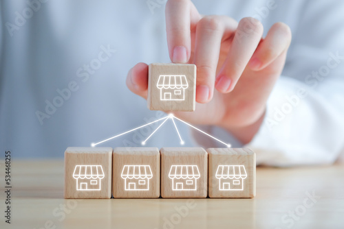Franchise Business marketing concept. Hand holding franchise store icon on wooden block with line network connection to another store. 