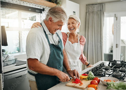 Senior couple, cooking and having fun while preparing a healthy food with vegetables for a vegan meal in the kitchen at home while laughing and having fun. Funny old man and woman helping with dinner