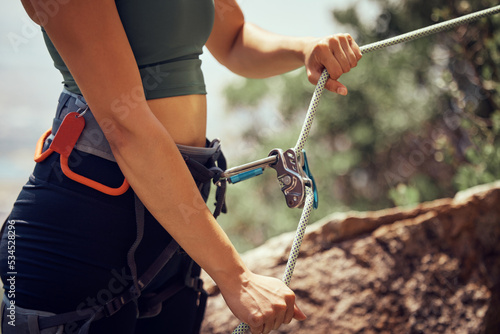 Fitness, safety and hands of rock climbing woman with security, harness cable or sport equipment on mountain cliff. Travel, hiking or adventure girl exercise with mountaineering rope workout training