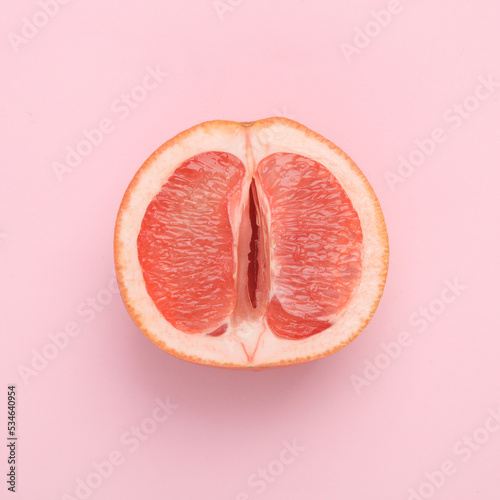 Gynecology, female intimate hygiene. Half of a ripe grapefruit symbolizing the female vagina on a pink background. Creative idea, allegory, fresh idea. Top view