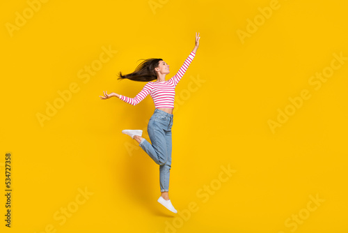 Full length photo of nice cheerful carefree girl dressed striped long sleeve jeans jumping flying isolated on yellow color background