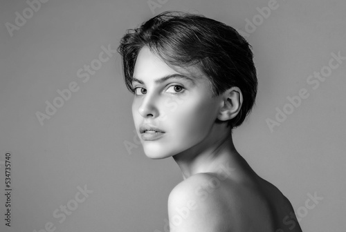 Monochrome portrait of a beautiful young woman with absolutely no makeup on a neutral gray background.