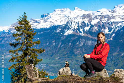 sweet woman with pigtails stands on top of a mountain in the swiss alps admiring the view of the snow-capped peaks; spring hike in the swiss alps, interlaken