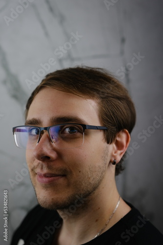 Unshorn and unshaven guy in glasses and black tshirt with long hair on gray background
