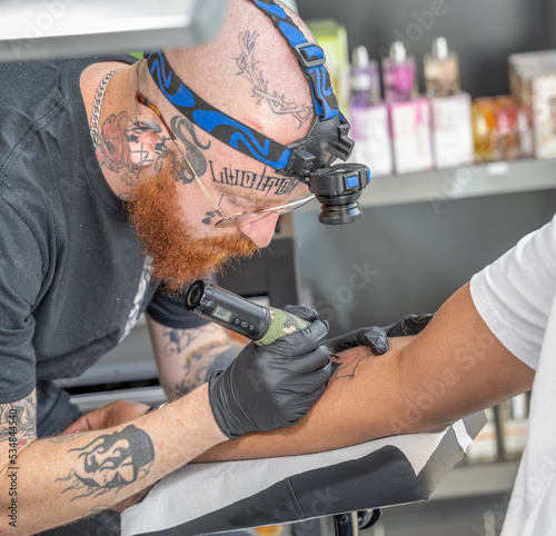 Tatoueur en pleine réalisation d'un tatouage sur le bas d'un client avec respect des règles d'hygiène
