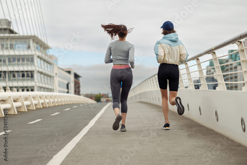 Two athletic women in sportswear is jogging on a bridge. Reaching the goal. Back view