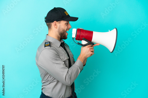 Young security man isolated on blue background shouting through a megaphone