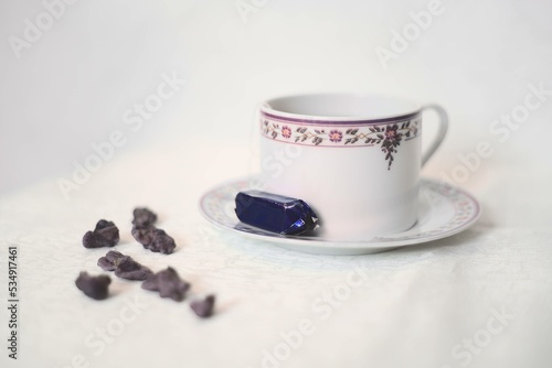 Tasse de thé violette et blanche avec des violettes cristallisées et un bonbon à la violette sur fond blanc style classique